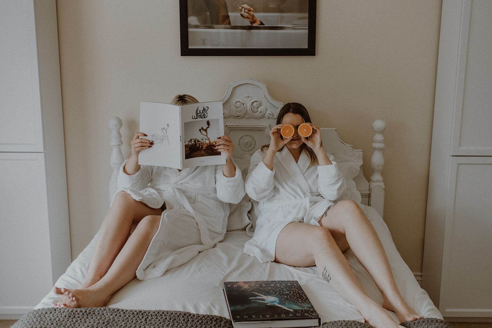 two girls in robes on a bed with coffee table books and oranges