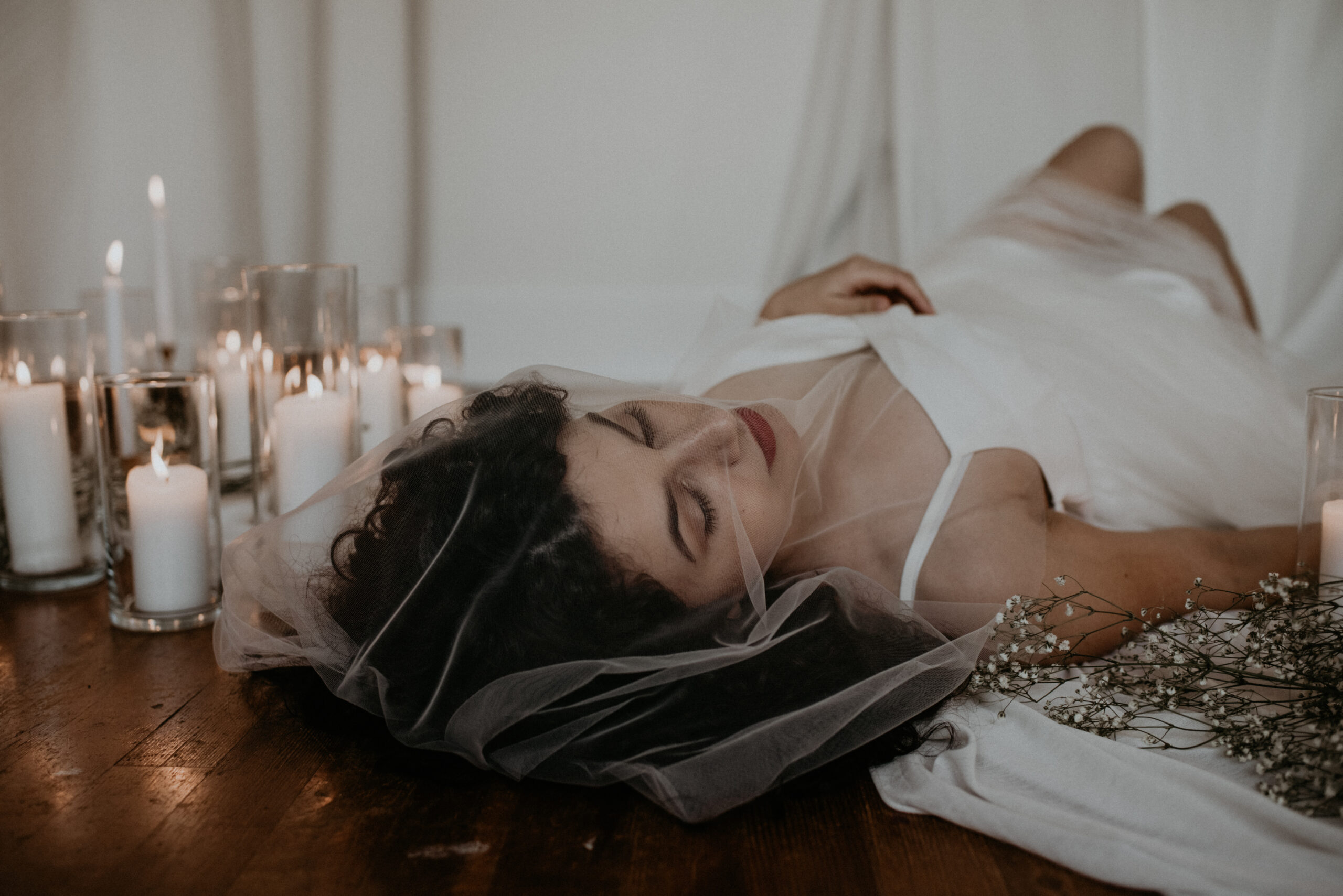 bride laying on the ground surrounded by candles with a veil over her face